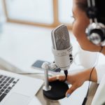 Persona con auriculares grabando un programa frente a un micrófono y un ordenador portátil para ilustrar la guía de SEO para podcast.