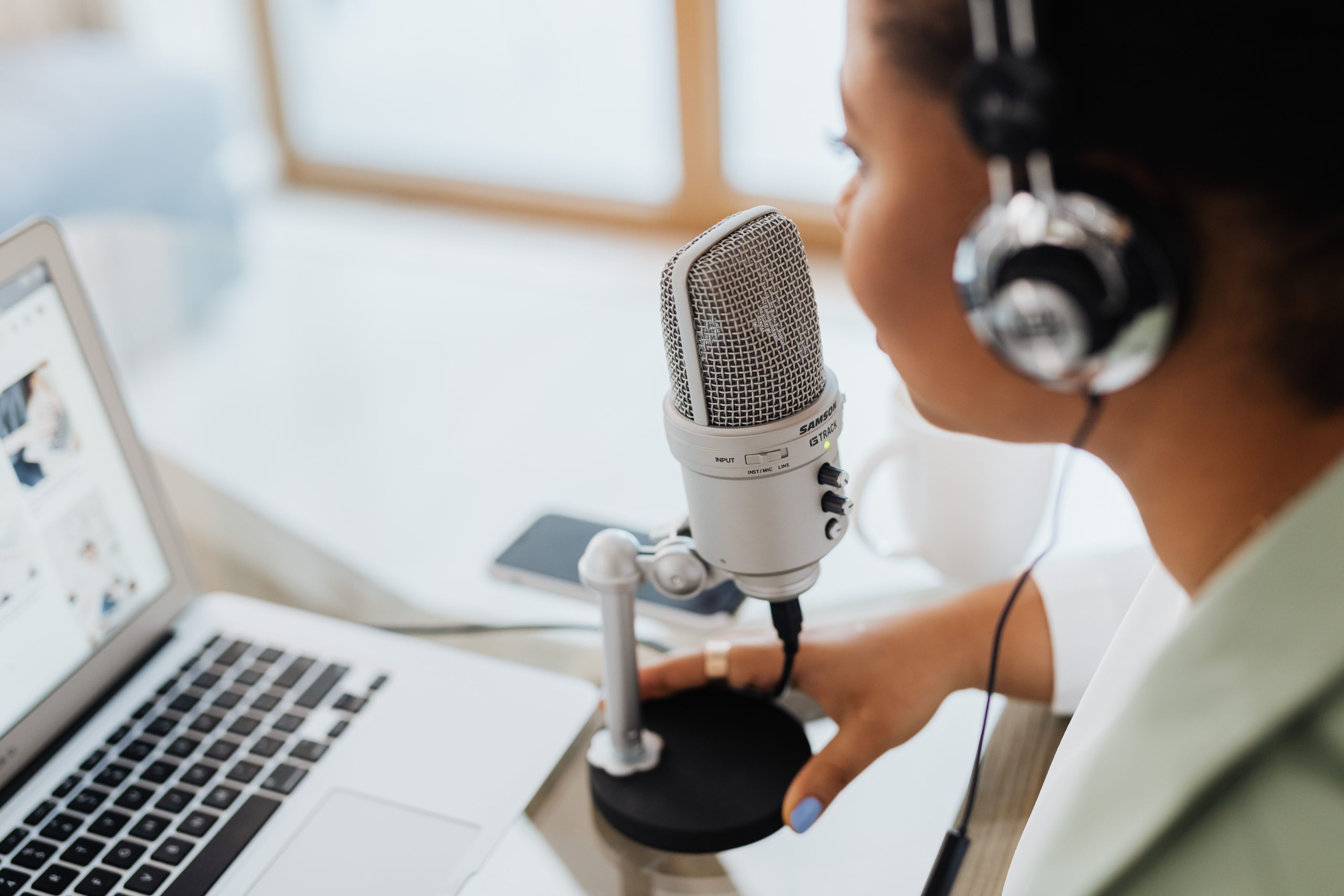 Persona con auriculares grabando un programa frente a un micrófono y un ordenador portátil para ilustrar la guía de SEO para podcast.
